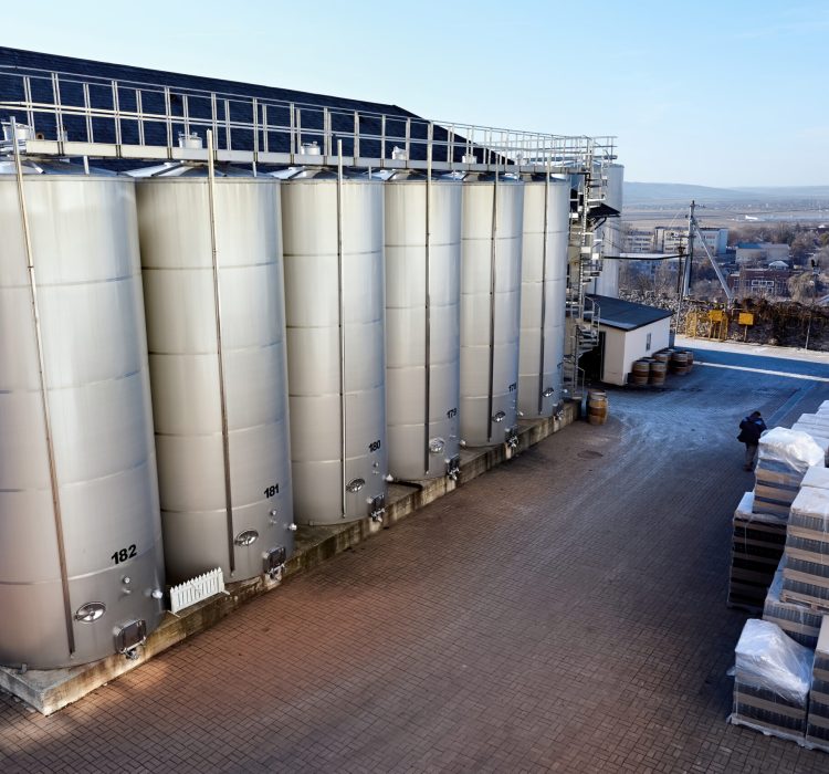 Metal wine storage tanks with dwelling houses on the background in a winery Metal wine storage tanks with dwelling houses on the background in a winery. Wide shot